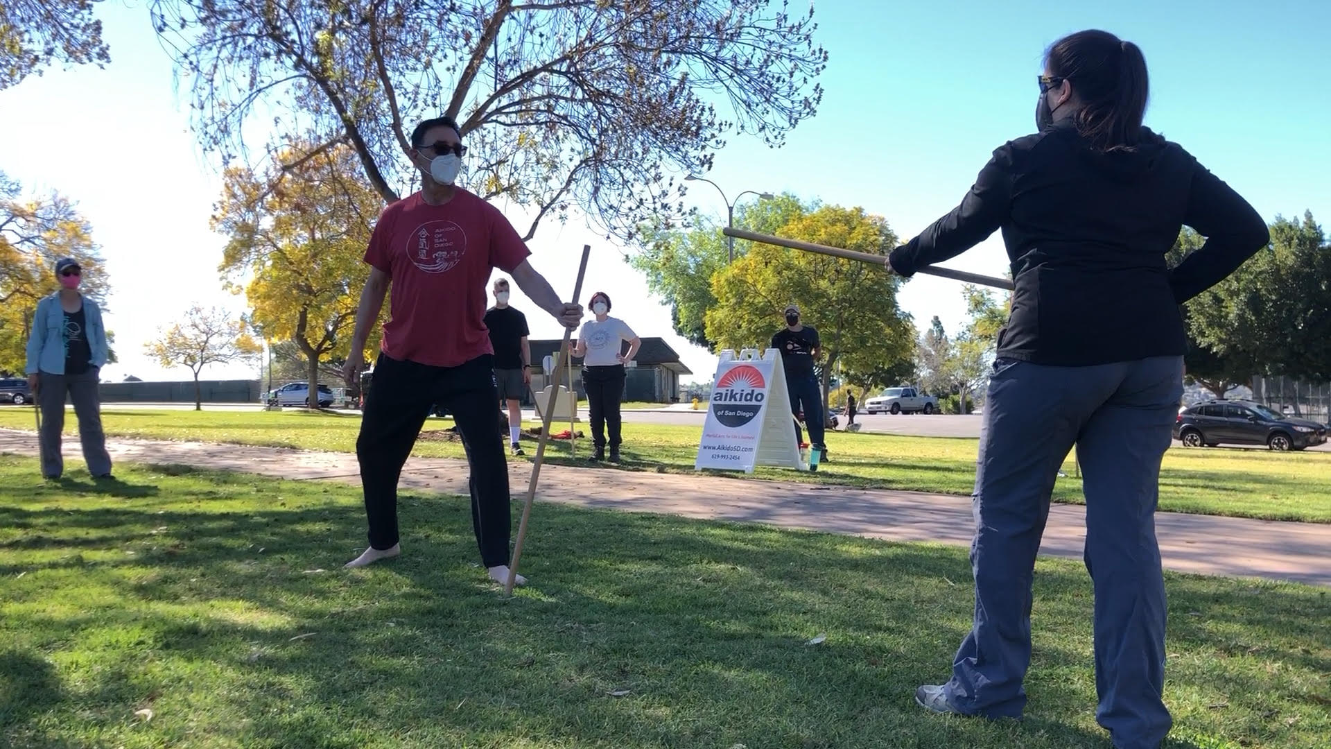 Sensei and a student training with wooden staffs in a sunny park
